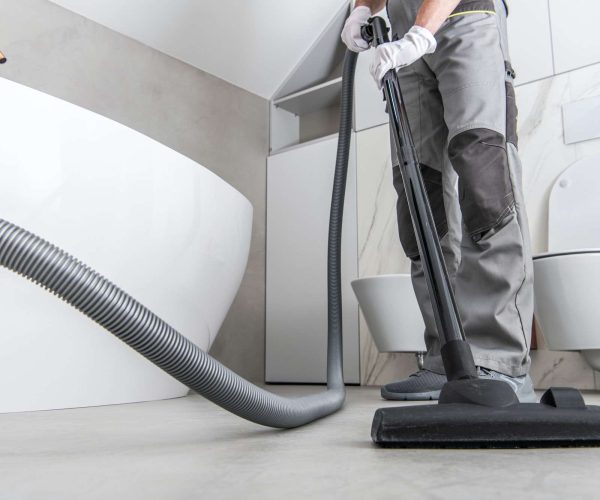 Man Vacuuming White Tile Floor In Bathroom.
