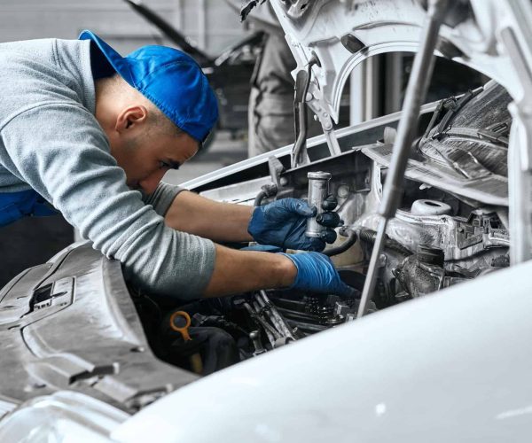 Mechanic in blue overalls checking serviceability of car engine